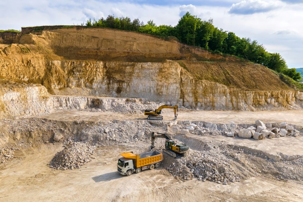 Open pit mining of construction sand stone materials with excavators and dump trucks.
